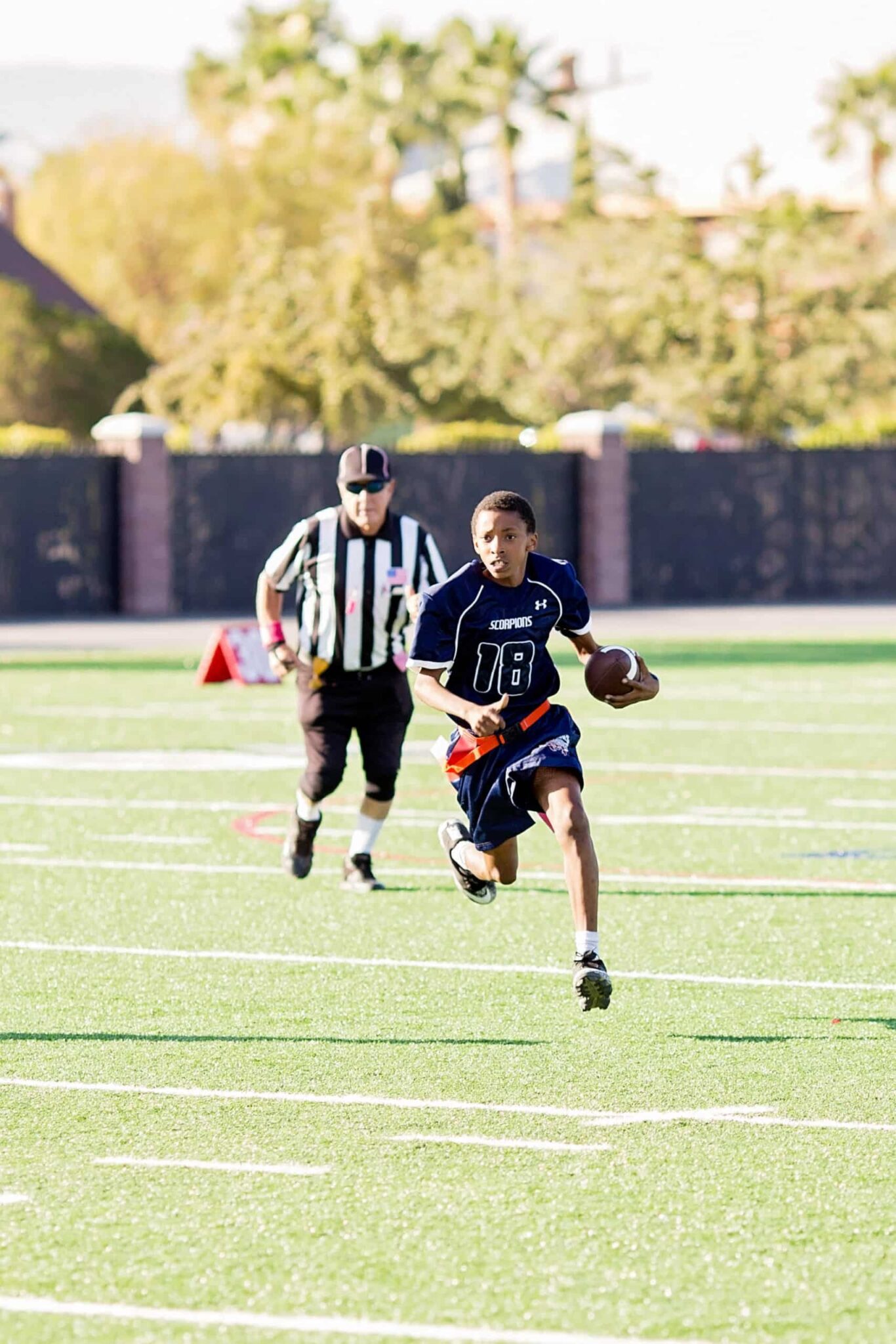 A young student football player runs with a football on a football field with a referee behind them