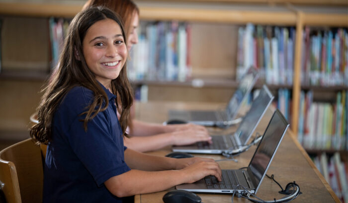 LVDS student on a laptop in the library and smiling at the camera
