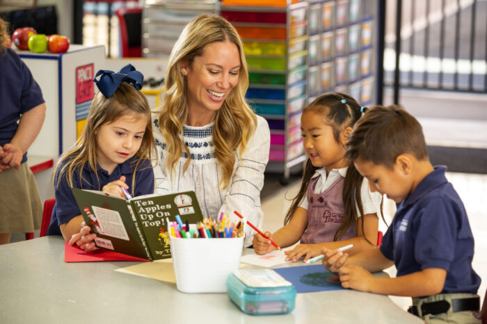a woman sitting in a Las Vegas Day School classroom smiling as she reads a dr suess book to two young students on either side of her