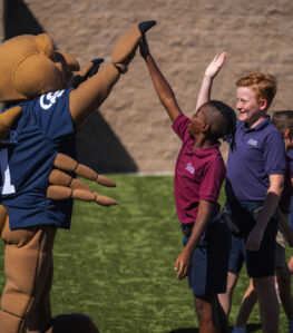 A person in a Scorpion mascot costume giving a high five to two young students