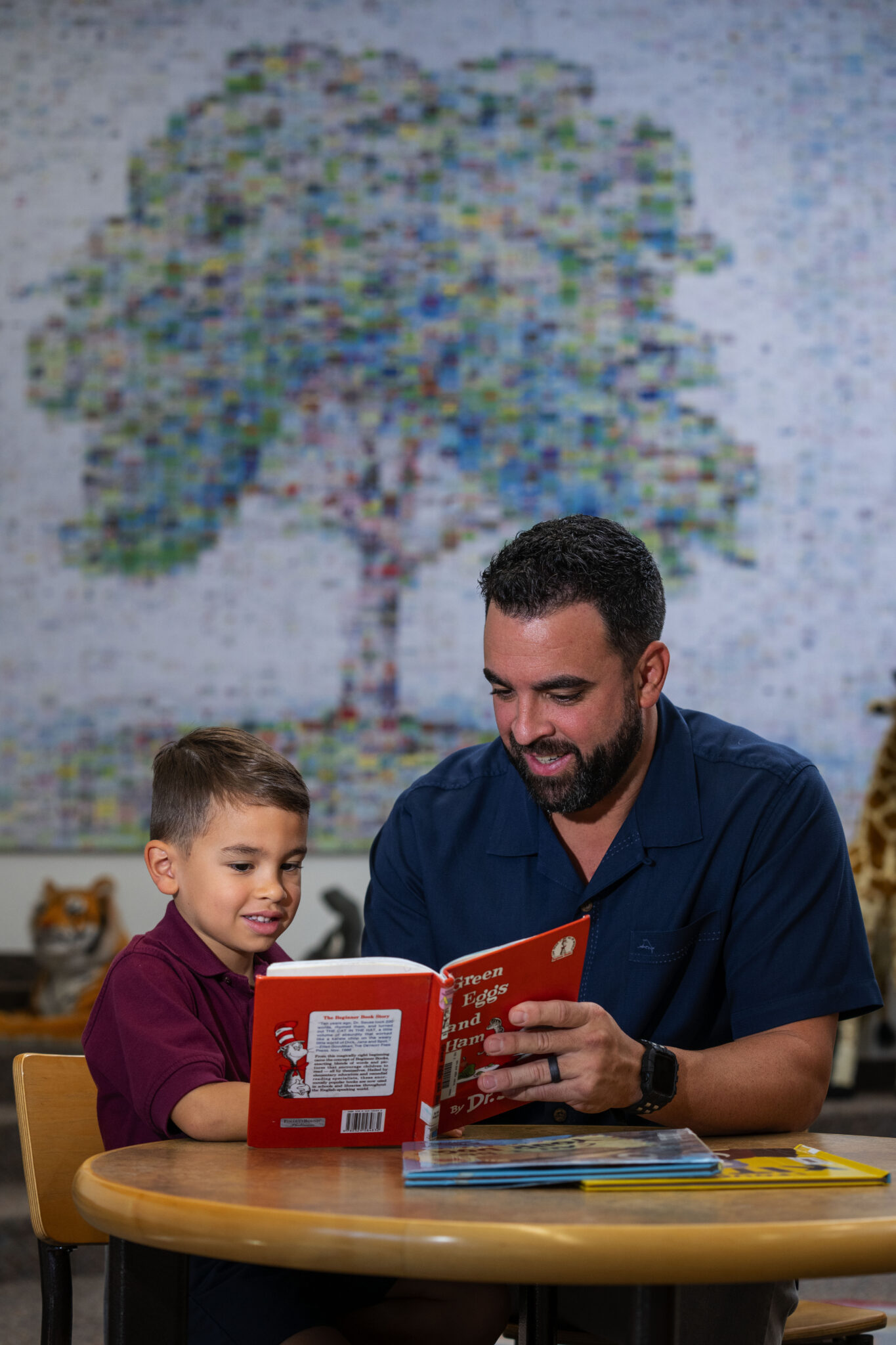 a man at a table reading Green Eggs and Ham with a young student